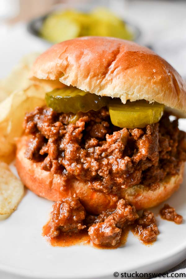 Up close shot of a sloppy Joe sandwich with pickles on a bun with chips