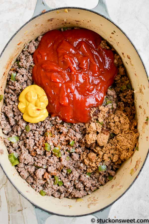 Ground beef in a dutch oven with ketchup, mustard, hot sauce, and brown sugar before being stirred.