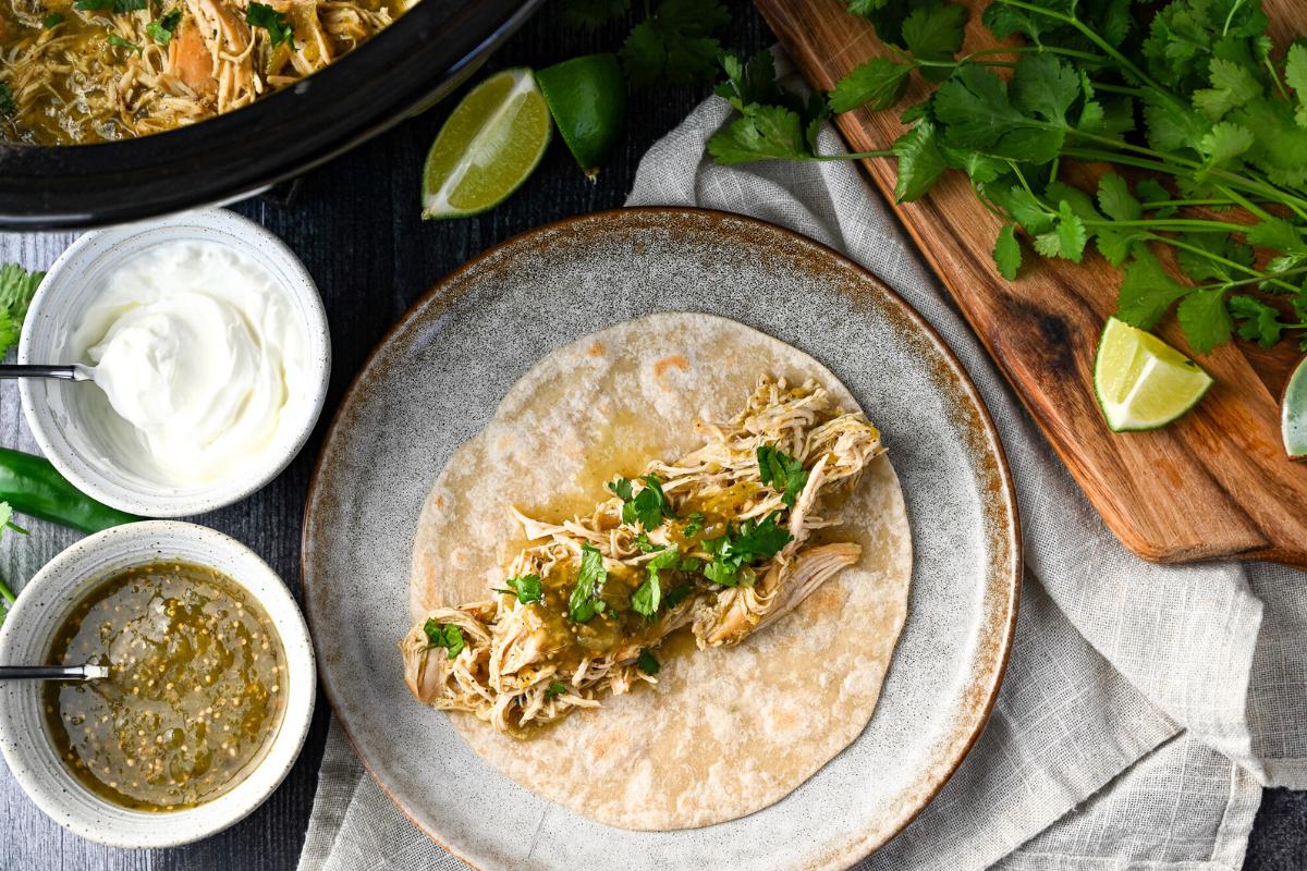 A plate featuring a shredded chicken taco adorned with cilantro and various garnishes