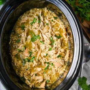 A close-up view of green chili chicken in a crockpot garnished with fresh cilantro