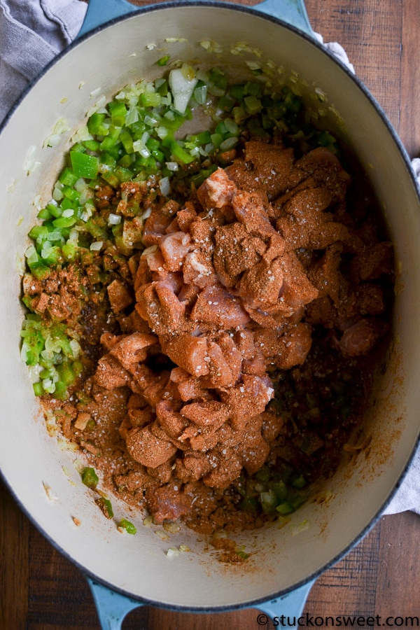 Diced onion and green pepper in a large Dutch oven with raw diced chicken and spices.