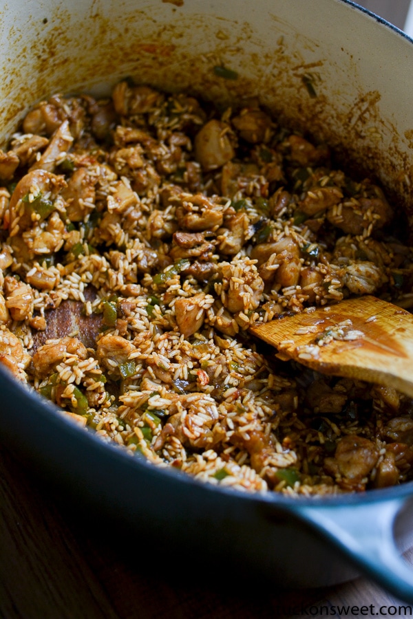 Diced onion and green pepper, diced chicken, and rice being combined in a Dutch oven using a wooden spoon.