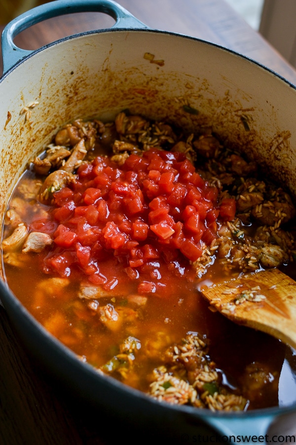 Diced tomatoes being added to the Mexican rice in a large Dutch oven.