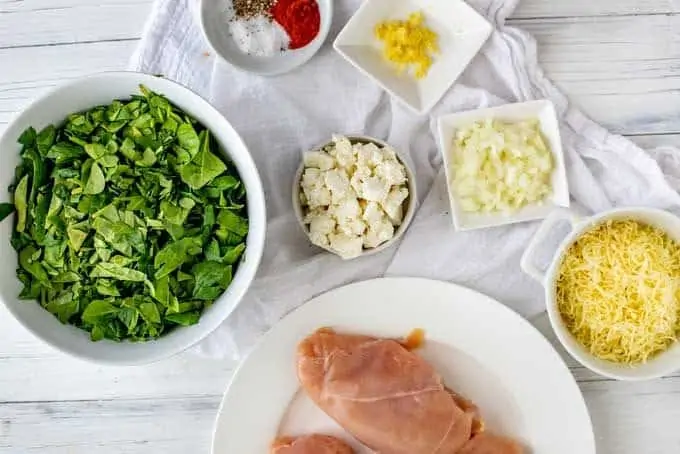 Ingredients for Keto Stuffed Chicken displayed in white preparation bowls on a white surface.