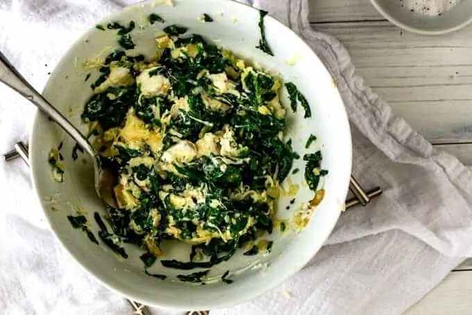 Image of combining spinach mixture and cheeses in a small white bowl.