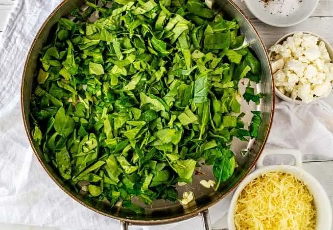 Image of spinach being added to a pan with sautéed onions.