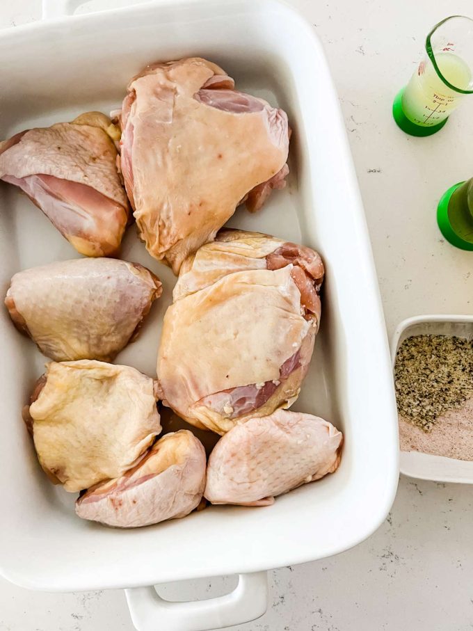 Overhead image of bone-in chicken thighs alongside lemon pepper, salt, lemon juice, and oil.