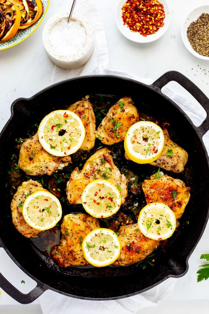 A cast iron skillet containing cooked lemon pepper chicken thighs garnished with parsley and lemon slices.