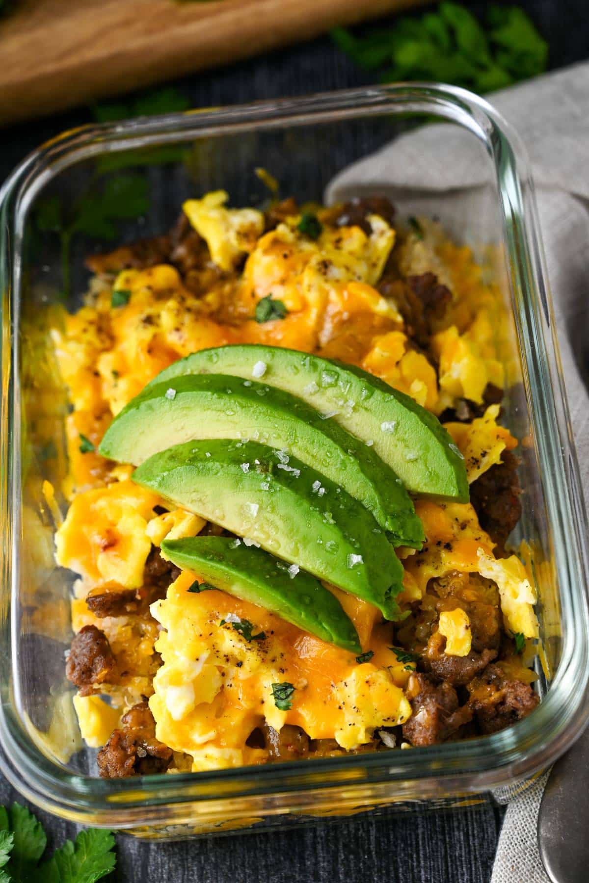 A breakfast bowl in a glass meal prep container, topped with sliced avocado.