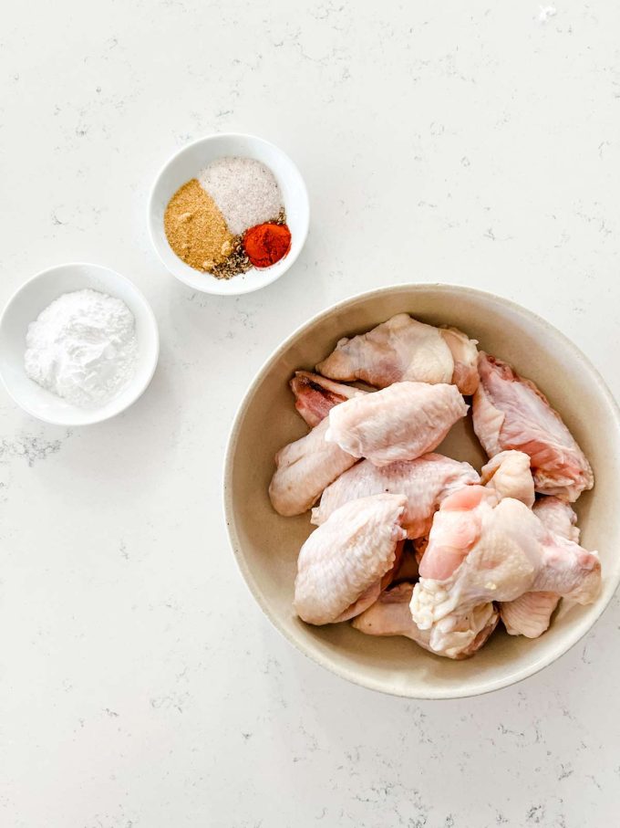 A top-down image of a bowl containing chicken flats and drumettes alongside seasonings and baking powder.