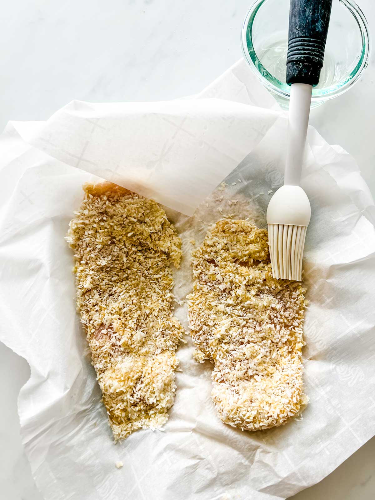 Crispy coconut chicken being brushed with coconut oil using a silicone brush.