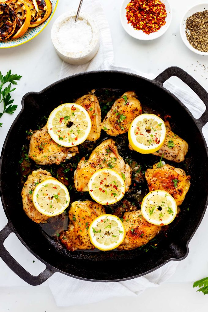 Overhead shot of a skillet featuring lemon pepper chicken thighs adorned with lemon slices.